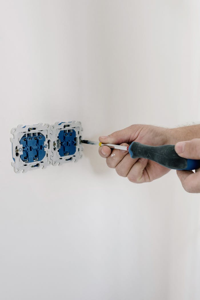 Home Close-up of hands using a screwdriver to install electrical sockets on a white wall.